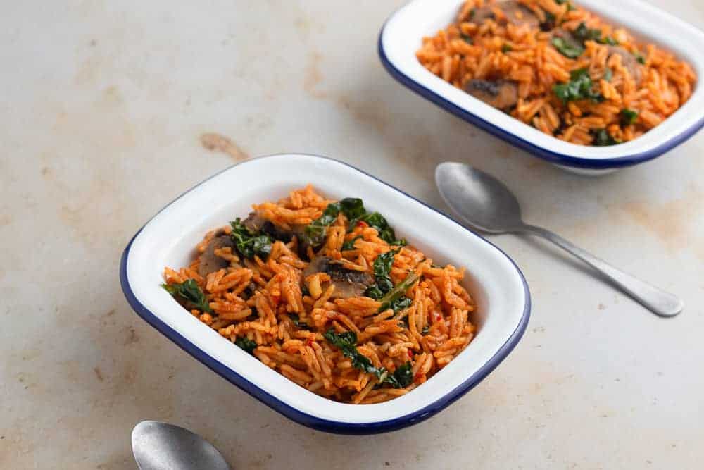 Vegetarian jollof rice with mushroom and kale in a bowl, with spoons on the side.