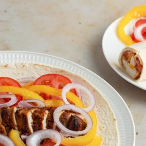 Tortilla wrap loaded with suya chicken, sliced onions, peppers and tomatoes