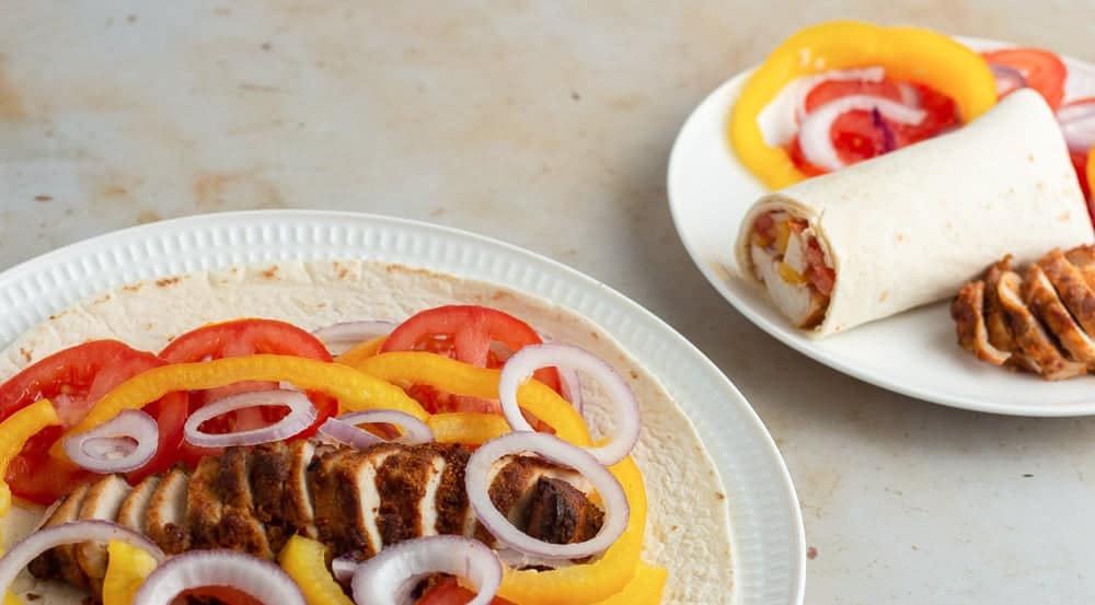 Tortilla wrap loaded with suya chicken, sliced onions, peppers and tomatoes