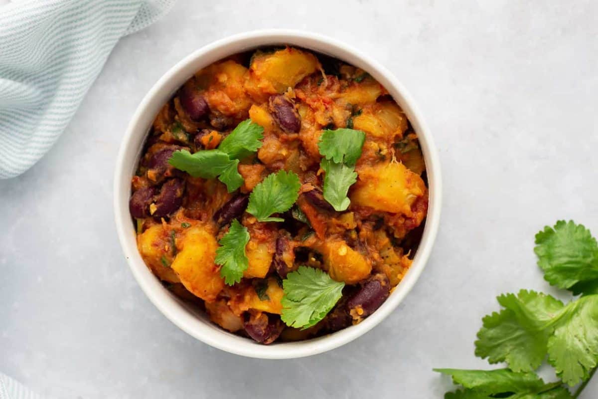 Matoke with beans in a bowl, with coriander garnish.