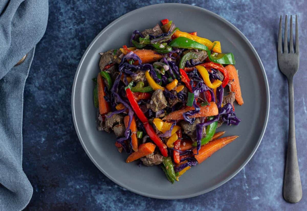 Asun meat with peppers, carrots and purple cabbage warm salad on a flat plate.
