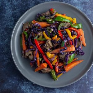 Asun meat with peppers, carrots and purple cabbage warm salad on a flat plate.
