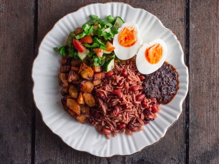 Waakye in a white plate with kelewele. shite, eggs and salad