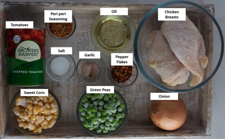 Ingredients for peri peri shredded chicken with vegetables laid out on a wooden tray.